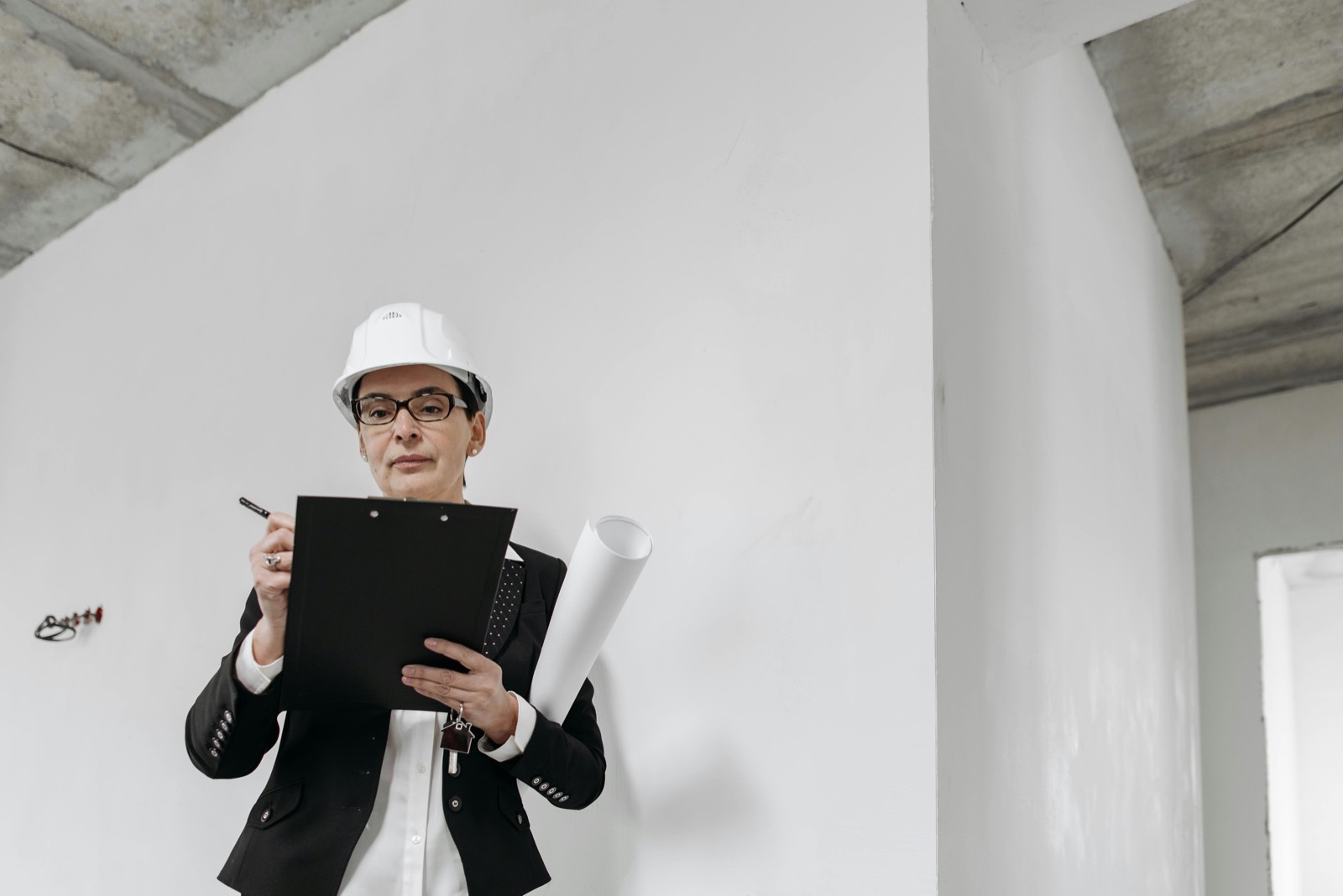 Rzeczoznawca w kasku ochronnym ogląda wnętrze nieruchomości z dokumentacją techniczną w ręku